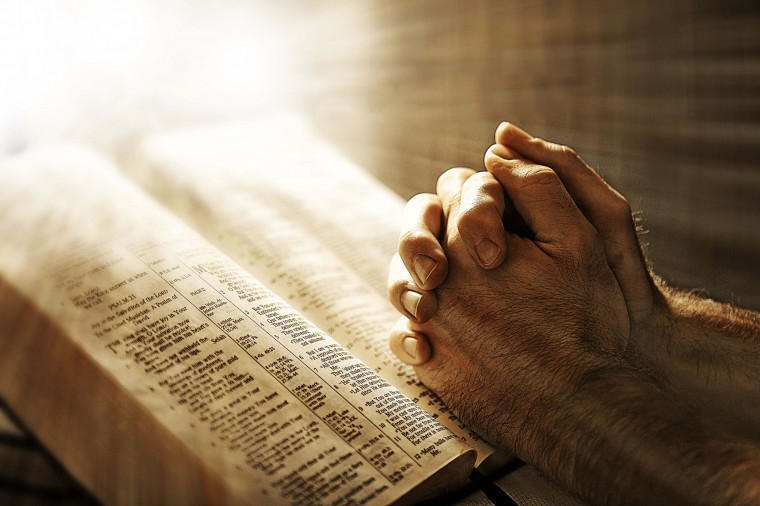 Light shining on praying hands toward open Bible